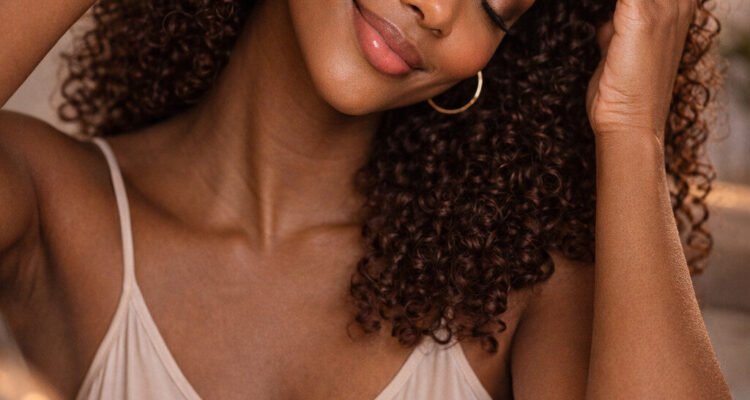 Black woman gently massaging her scalp with glowing hair and peaceful smile